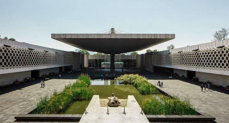 Large concrete umbrella structure over a central courtyard with a pond and geometric patterned walls.